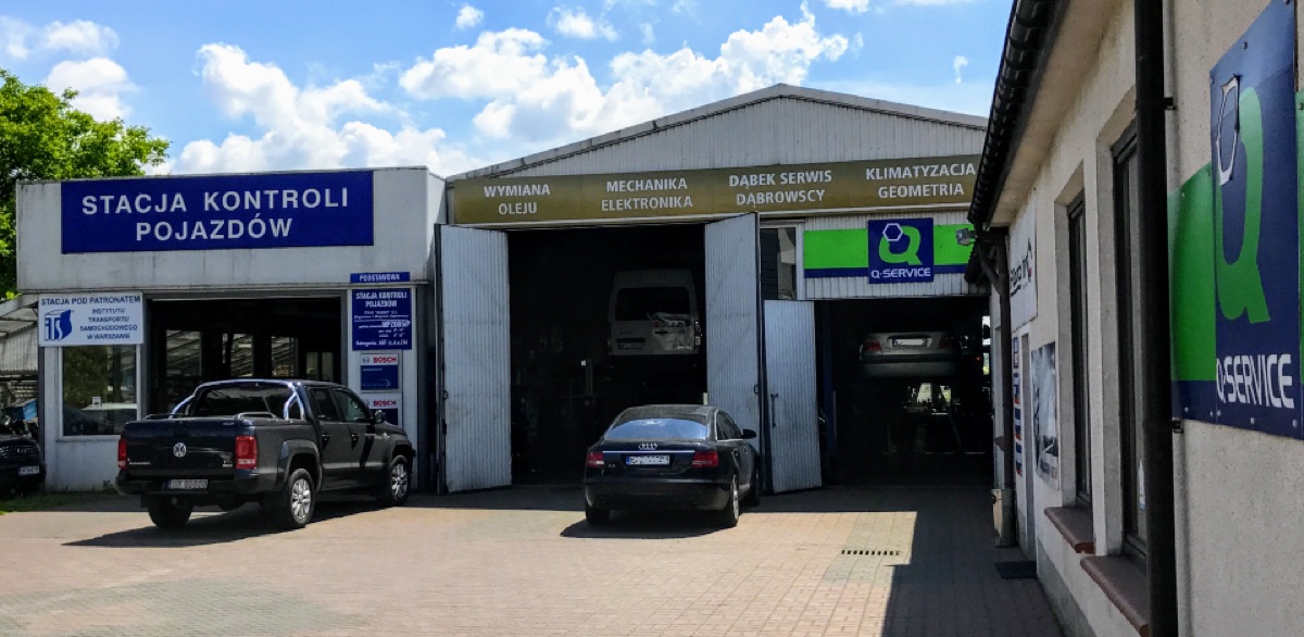 Warsztat P.H.U. Dąbek w Przasnyszu: budynek stacji kontroli pojazdów, hala serwisowa z otwartymi bramami i samochodami na podnośnikach oraz szyld Q Service